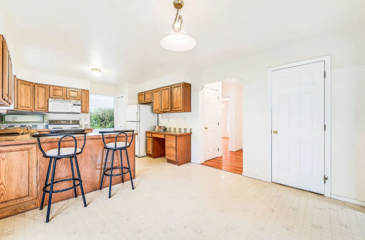 Open kitchen interior with wood cabinets, bar seating, and white flooring